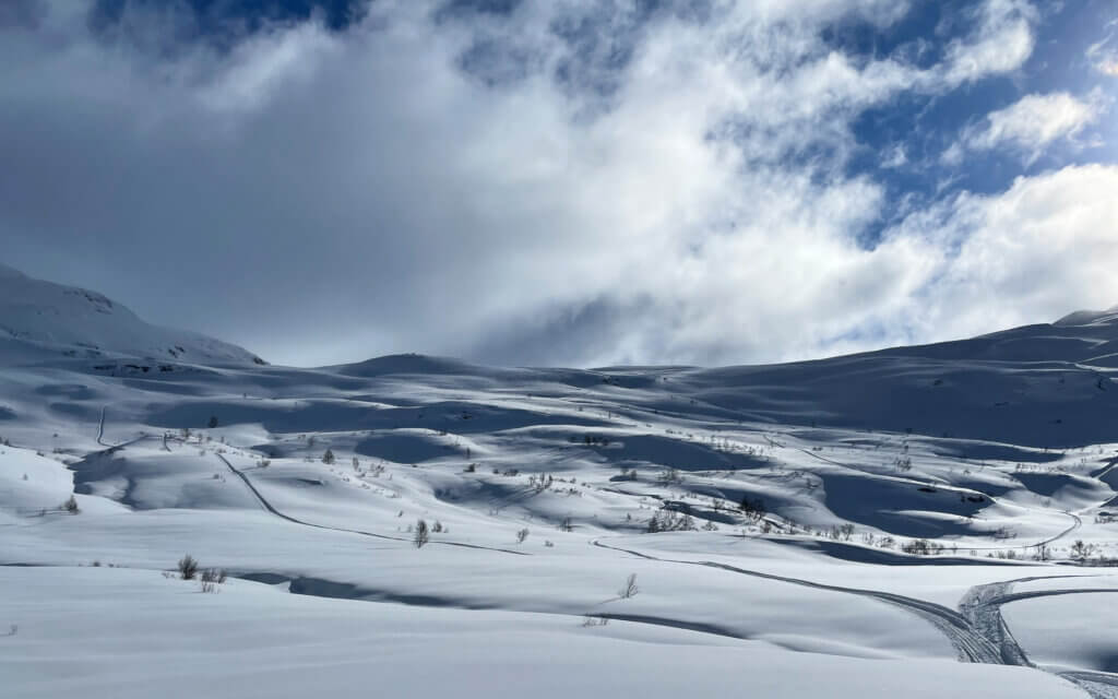 Maldal i snø med blå himmel og skyer.