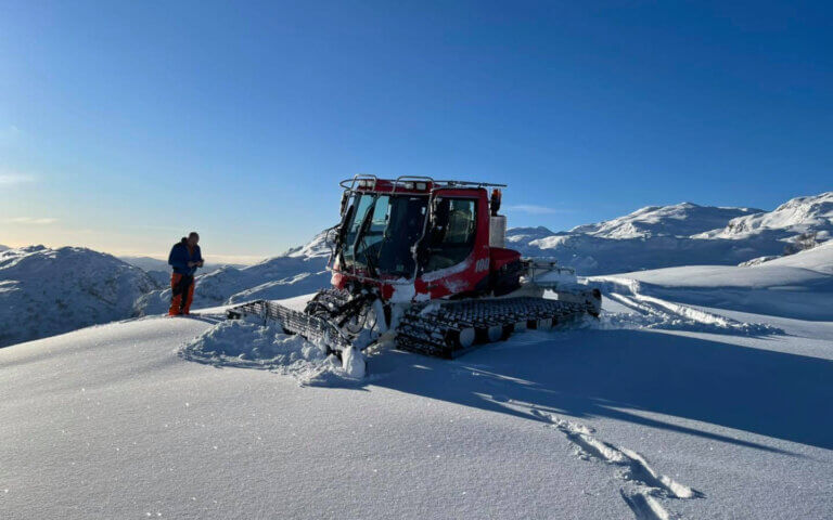 A snow tracker machine on a mountaintop in Svandalen in snow and blue skies.