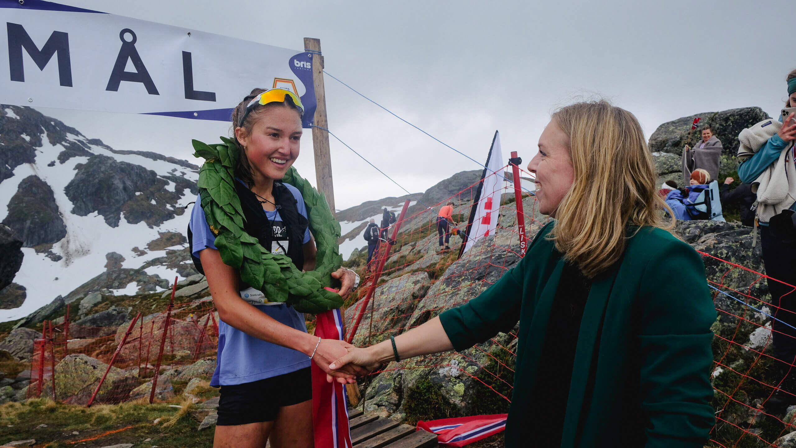 A woman greeting another woman with a winner's wreath around her shoulders on top of Hovlandsnuten.