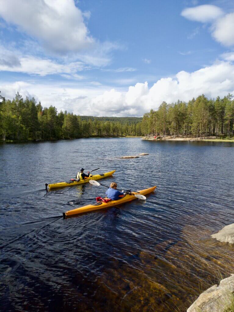 Two people kayak in a mountain lake in summer.