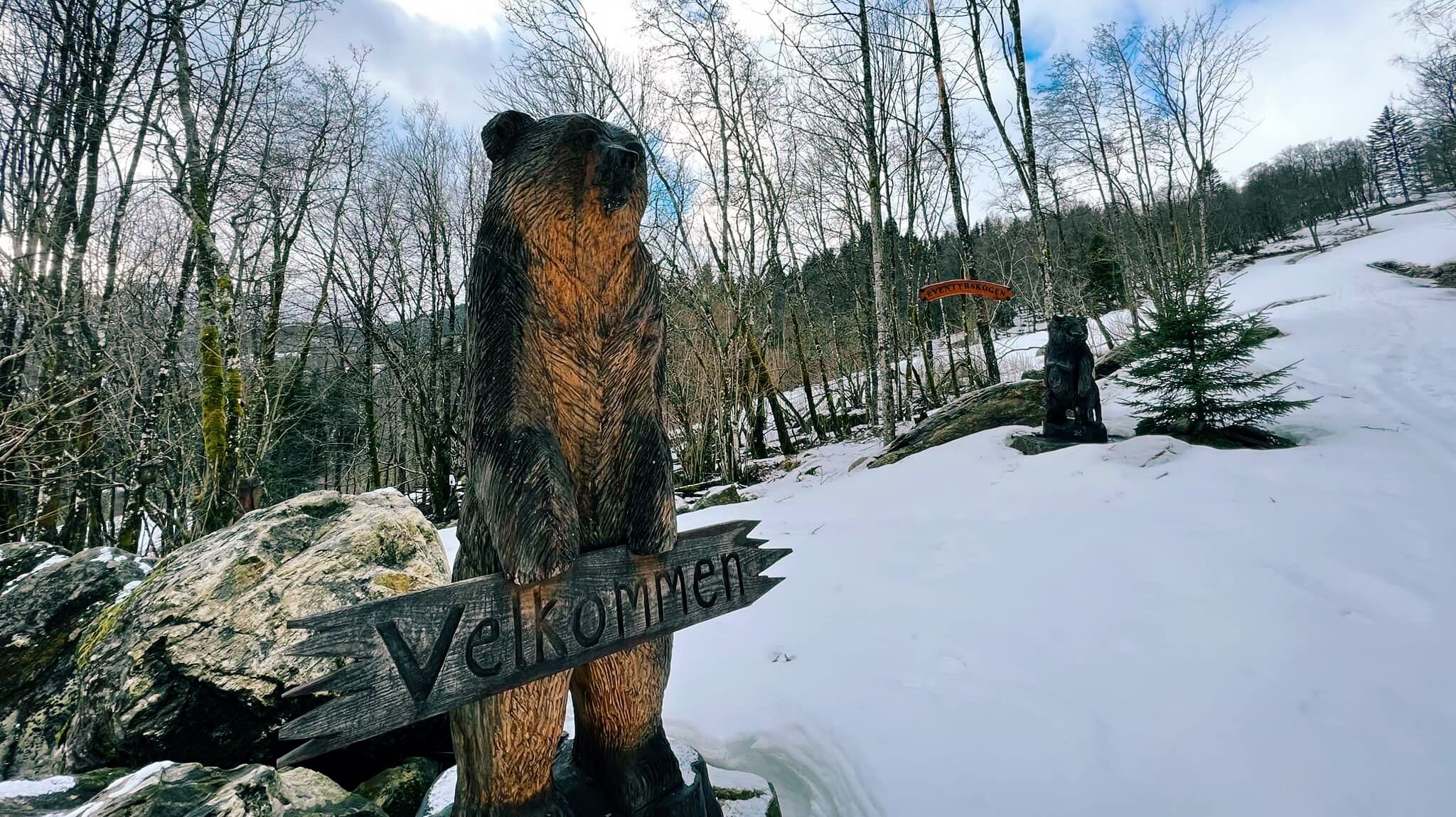 Treskulptur av ein bjørn held eit velkommen skilt på Eventyrplassen i Sauda.