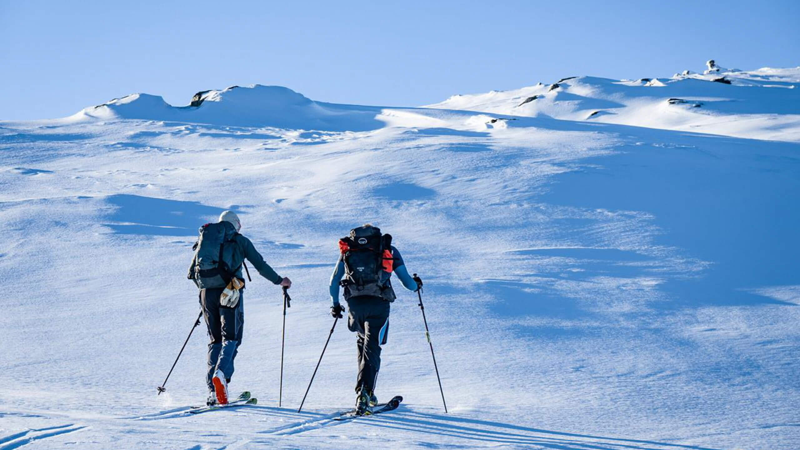 To skigåere med ryggsekker på topptur en klar vintersdag.