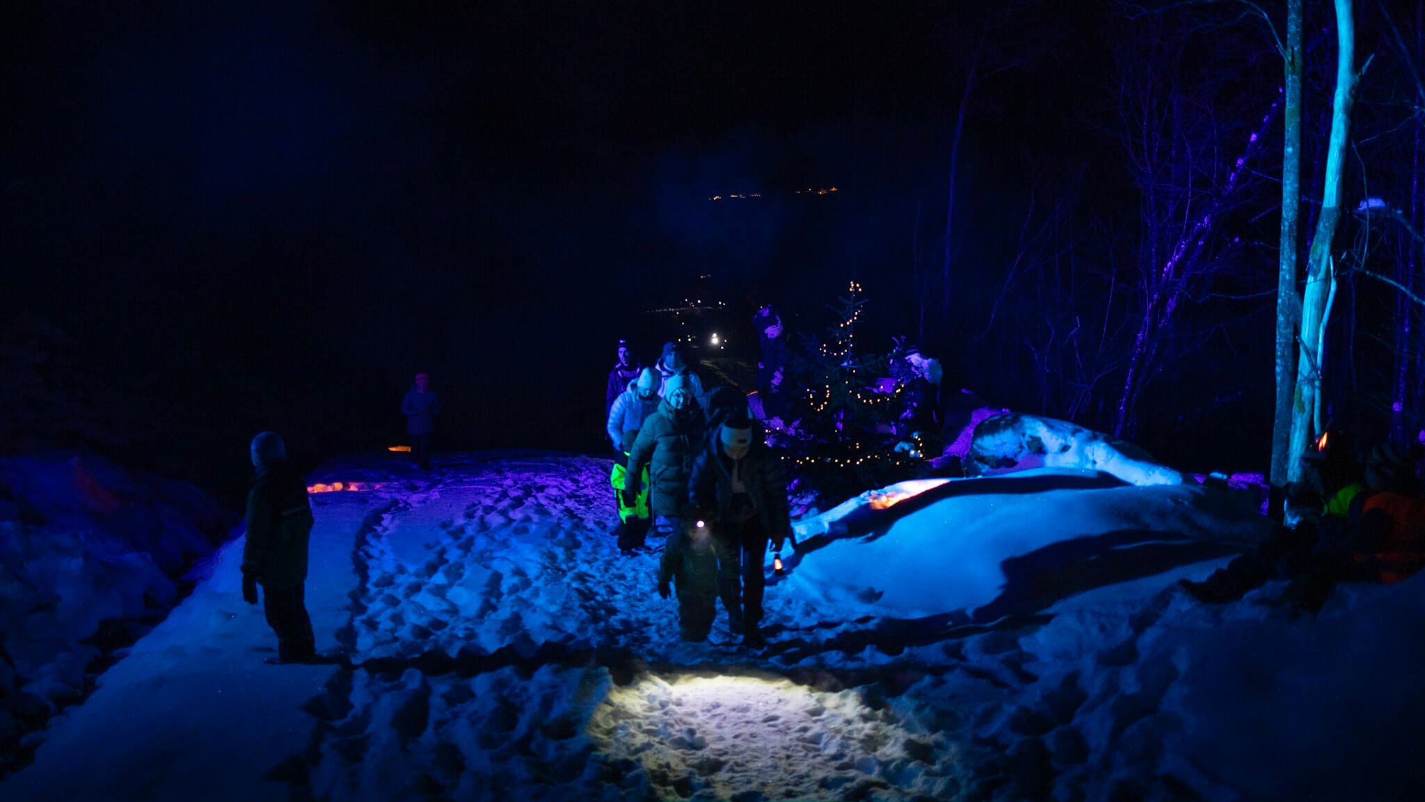 Bilde av Eventyrskogen på kvelden i snø med folk med hodelykter som går opp stien.