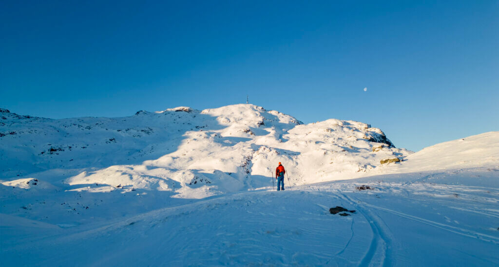 Ein skigåar på veg til Ravnafjell på ein dag med blå himmel.