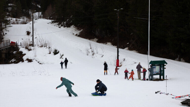 Barn og voksne i et snøområde koser seg med akebrett og ski